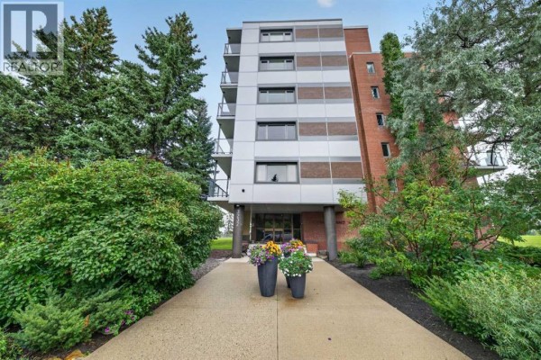 Front entrance of an apartment building with trees, bushes, and decorative planters. - 506 507, 3232 Rideau Place Sw, Calgary