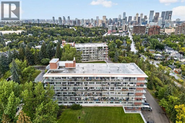 Aerial view of apartment buildings with surrounding trees and distant city skyline. - 506 507, 3232 Rideau Place Sw, Calgary