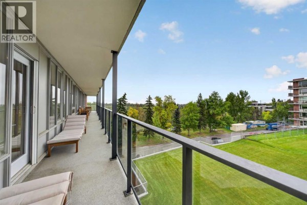Long balcony with lounge chairs overlooking a grassy field and trees. - 506 507, 3232 Rideau Place Sw, Calgary