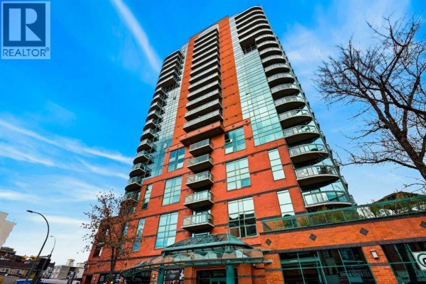 Low angle view of the brick and glass apartment building exterior with balconies and blue sky. - 507, 836 15 Avenue Sw, Calgary