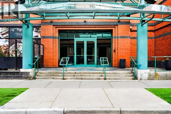 Covered entrance to the apartment building with glass doors, brick walls, and teal accents. - 507, 836 15 Avenue Sw, Calgary