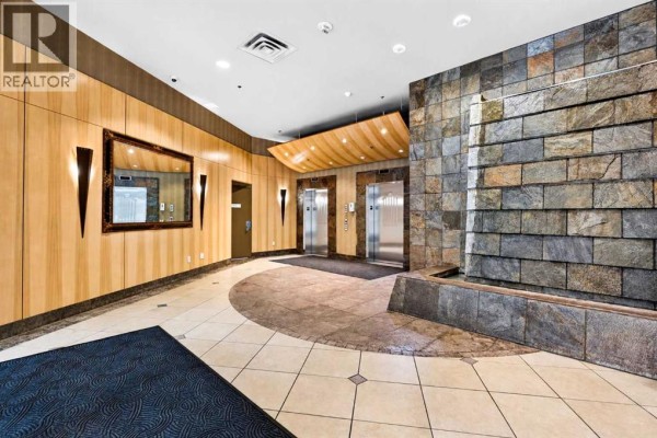 Apartment building lobby with elevators, tiled floor, a stone accent wall with a water feature, and wood paneling. - 507, 836 15 Avenue Sw, Calgary