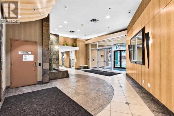 Wide view of the apartment building lobby, showing elevators, entrance doors, stone and wood finishes, and a water feature. - 507, 836 15 Avenue Sw, Calgary