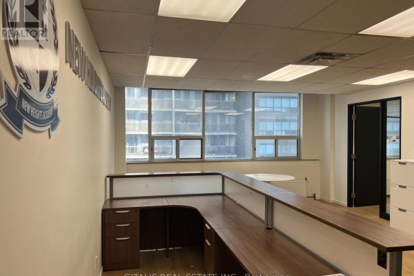 Office interior with a large reception desk, windows, and a door leading to another office. - 507 - 27 Carlton Street, Toronto