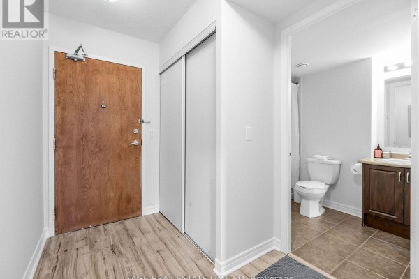 Apartment hallway with a wood-grain door, closet, and view into a bathroom. - 507 - 60 Fairfax Crescent, Toronto