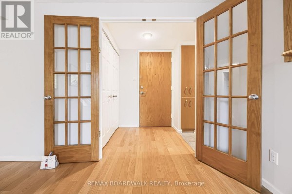 Interior hallway with light hardwood floors, white walls, and double wooden doors with glass. - 507 - 960 Teron Road, Ottawa