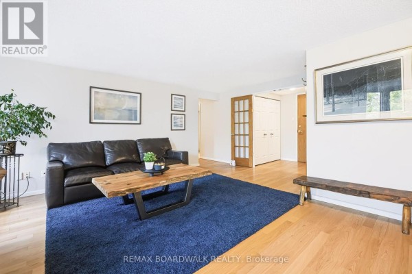 Living room with a dark leather sofa, wooden coffee table, blue rug, and hardwood floors. - 507 - 960 Teron Road, Ottawa