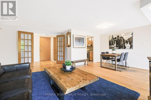 Living and dining area with hardwood floors, a dark sofa, wooden table, and chairs. - 507 - 960 Teron Road, Ottawa