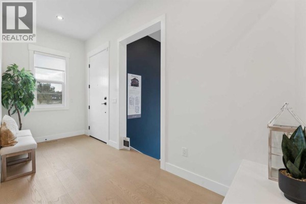 Entrance hallway with white walls, light wood floors, and a door leading to a dark blue accent wall area. - 507 Waterford Rise, Chestermere