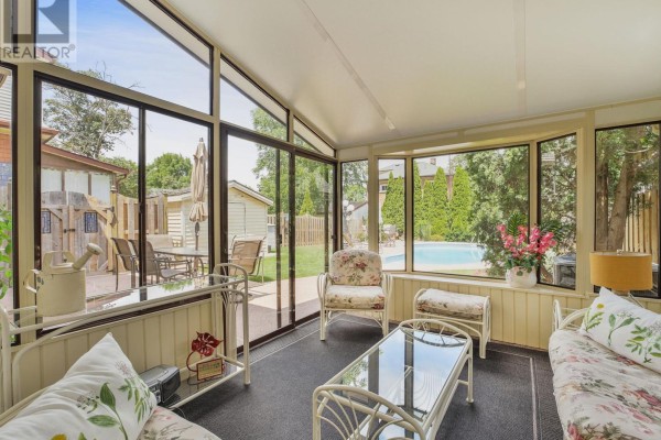 Backyard patio with a glass table and chairs, a sunroom, and an oval swimming pool. - 5079 Armoury Street, Niagara Falls