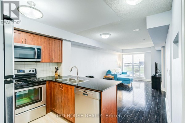 Kitchen and living area with dark hardwood floors, cherry wood cabinets, and a blue sofa. - 508 - 1070 Sheppard Avenue W, Toronto
