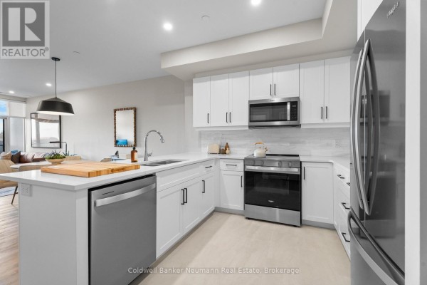 Kitchen with white cabinets, stainless steel appliances, and a large island with sink. - 508 - 1882 Gordon Street, Guelph