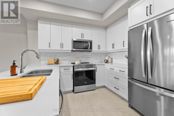 Kitchen with white cabinets, stainless steel appliances, and view into the living area. - 508 - 1882 Gordon Street, Guelph