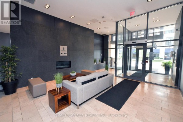Apartment building lobby with a modern fireplace, grey sofas, and glass-enclosed entrance. - 508 - 1940 Ironstone Drive, Burlington
