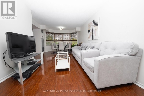 Living and dining room with light gray sofas, wooden floors, and bay windows. - 508 - 325 Webb Drive, Mississauga