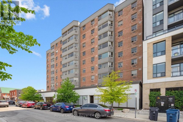 Exterior view of a multi-story brick apartment building with surrounding trees and cars. - 508 - 55 Yarmouth Street, Guelph