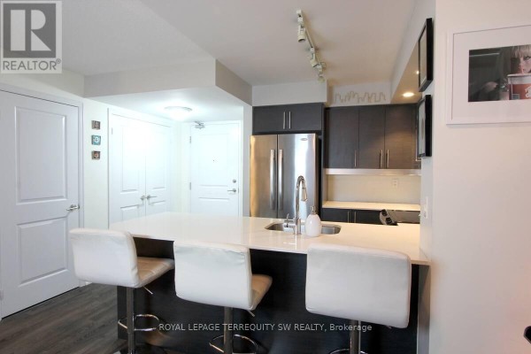 Kitchen with stainless steel appliances, dark cabinetry, and a white quartz island. - 508 - 65 East Liberty Street, Toronto