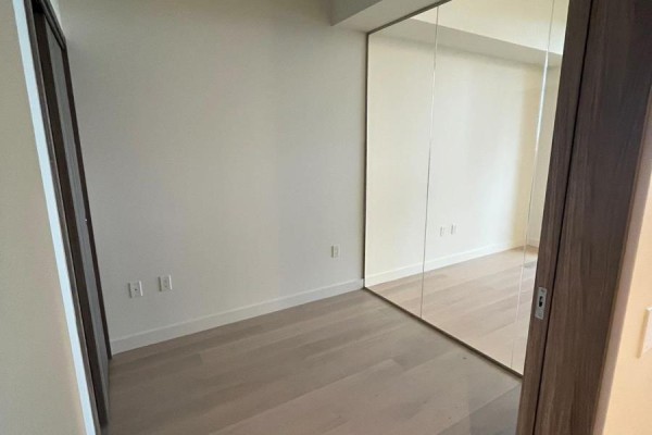 Empty room with light wood floors and mirrored closet doors. - 508 - 95 Mcmahon Drive, Toronto