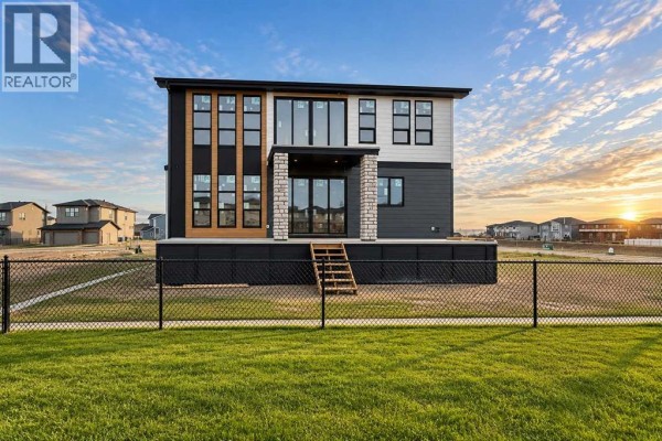 Rear exterior view of a modern house with a dark grey and white facade, large windows, and a wooden deck. - 508 South Shore Link, Chestermere