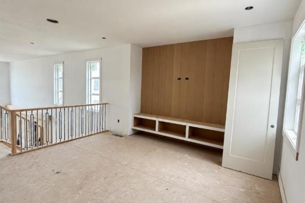 Interior view of an unfinished room with white walls, a wood-paneled feature wall with open shelving, and a closed white door. - 508 South Shore Link, Chestermere