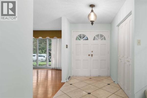 Foyer with double white doors, tiled floor, and a view into the living room. - 508 Willow Brook Drive Se, Calgary