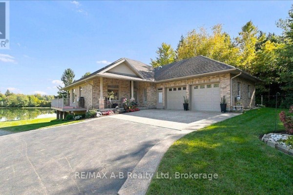 Brick house with a double garage and a deck overlooking a pond. - 5083 Perth 107 Road, Perth East