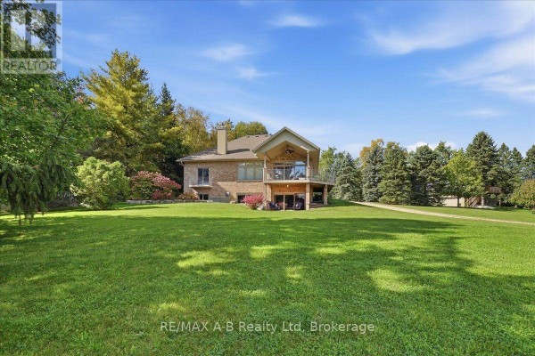 Rear view of a brick house with a large backyard and treed surroundings. - 5083 Perth 107 Road, Perth East