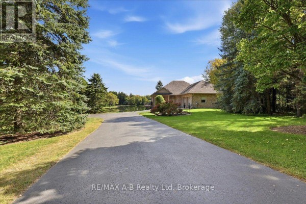 Asphalt driveway leading to a brick house surrounded by mature trees and lawn. - 5083 Perth 107 Road, Perth East