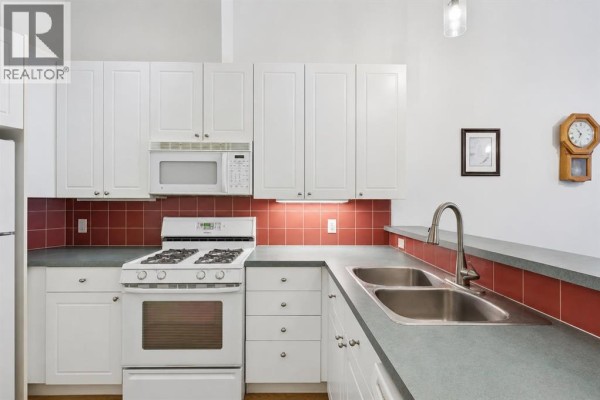 U-shaped kitchen with white cabinets, white appliances, red tile backsplash, and stainless steel double sink. - 509, 923 15 Avenue Sw, Calgary