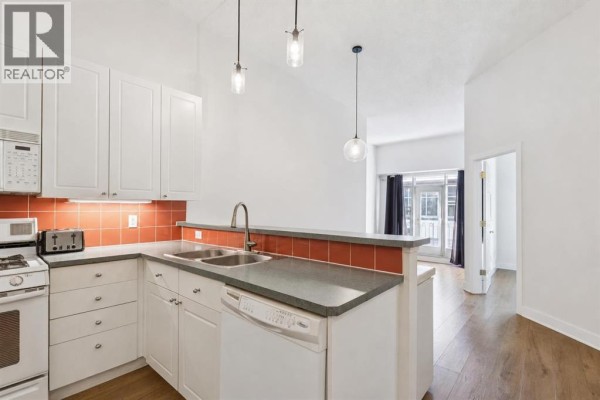 Open-concept kitchen and living area, showing white cabinets, red tile backsplash, and balcony view. - 509, 923 15 Avenue Sw, Calgary