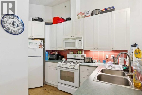 Corner kitchen with white cabinets, white appliances, red tile backsplash, and stainless steel double sink. - 509, 923 15 Avenue Sw, Calgary