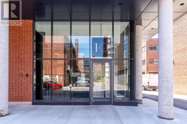 Building entrance with large glass windows, doors, and concrete pillars. - 509 - 10 James Street, Ottawa