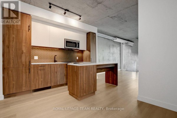Modern apartment kitchen with walnut cabinets, stainless steel appliances, and concrete ceiling. - 509 - 10 James Street, Ottawa