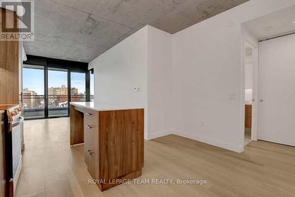 Open concept apartment living area with kitchen island, hardwood floors, and city view. - 509 - 10 James Street, Ottawa