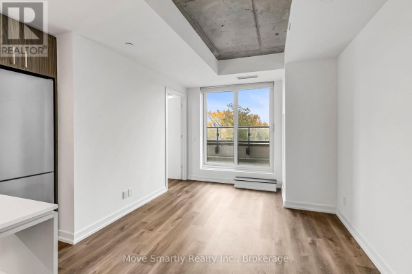 Living area with white walls, wood floors, and a view of trees through a large window. - 509 - 115 Larchmount Avenue, Toronto