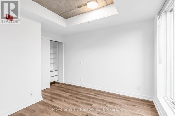 Empty bedroom with white walls, wood floors, and a sliding door closet. - 509 - 115 Larchmount Avenue, Toronto