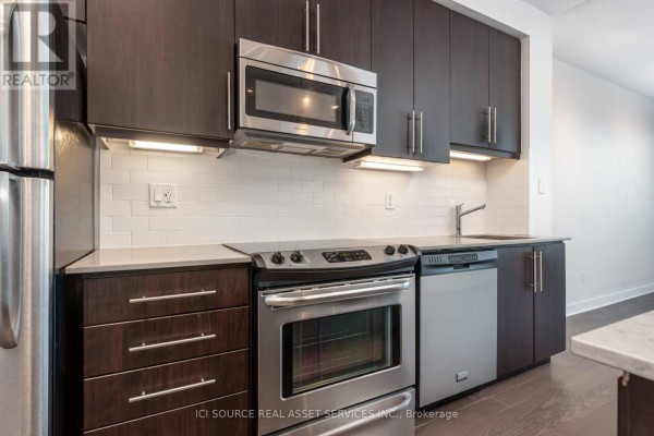 Open concept living area with dark hardwood floors, a kitchen island, and a glass-doored bathroom. - 509 - 1169 Queen Street W, Toronto