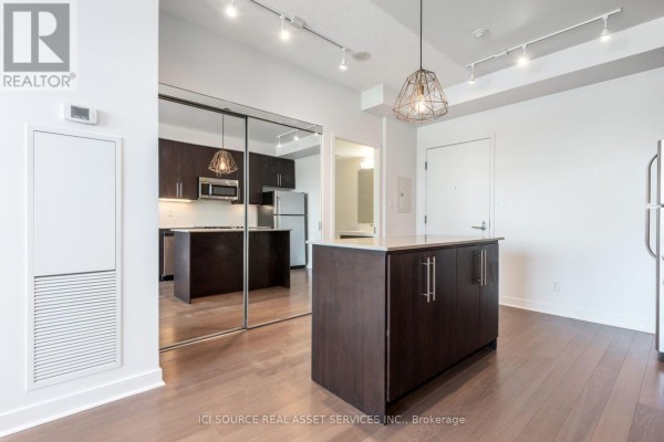 Empty room with dark hardwood floors and a large window wall offering a city view. - 509 - 1169 Queen Street W, Toronto