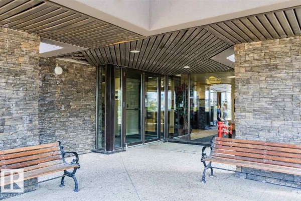 Entrance to apartment building with stone facade, glass doors, and wooden benches. - #509 10149 Saskatchewan Dr Nw, Edmonton