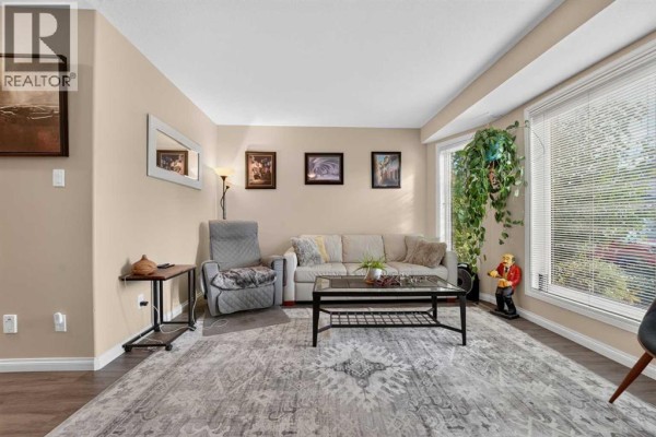 Living room with beige walls, a sofa, armchair, coffee table, and large bay windows. - 509 Gateway Crescent S, Lethbridge