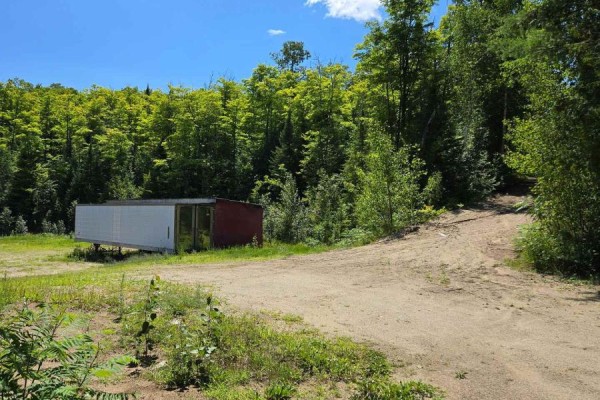 A trailer with a red end sits in a clearing next to a dirt road and a treeline. - 509 Road Road, Frontenac