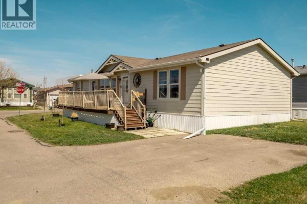 Right side exterior of a mobile home with beige siding and a concrete driveway in front. - 509 Station Street, Coaldale