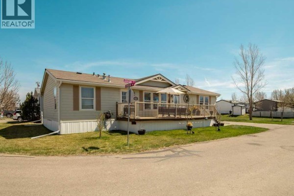 View of the right side of a mobile home with a wooden deck and beige siding. - 509 Station Street, Coaldale