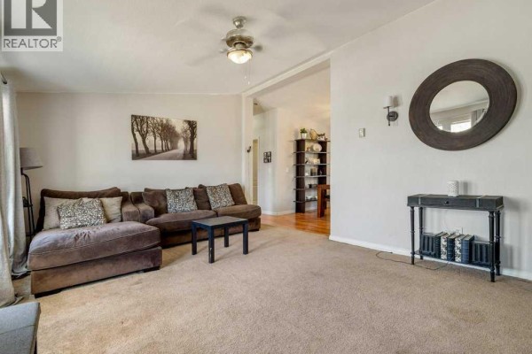 Living room with a large brown sectional sofa, beige carpet, and a decorative mirror on the wall. - 509 Station Street, Coaldale