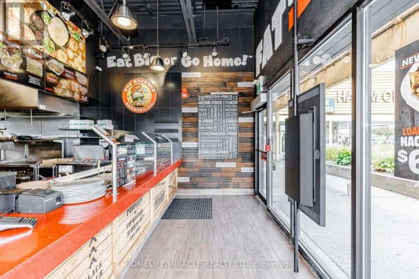 Restaurant counter area with orange countertop, menu boards, kitchen equipment, and a glass door. - 5095 Sheppard Avenue E, Toronto