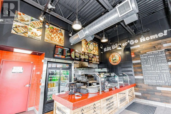 Commercial kitchen interior with stainless steel appliances, a refrigerator, counter space, and menu boards on black walls. - 5095 Sheppard Avenue E, Toronto