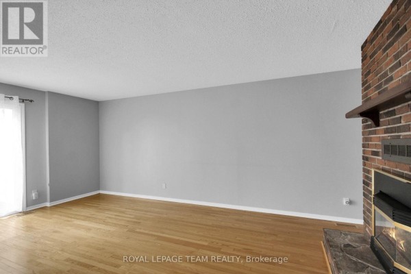 Living room with light hardwood floors, grey walls, and a brick fireplace. - 51 - 3240 Southgate Road, Ottawa