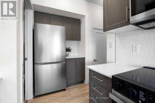 Kitchen with dark grey cabinets, a stainless steel refrigerator, and white hexagonal tile. - 51 - 940 St David Street N, Centre Wellington