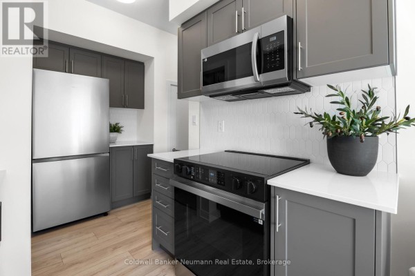 Kitchen with dark grey cabinets, stainless steel appliances, and a white geometric tile backsplash. - 51 - 940 St David Street N, Centre Wellington