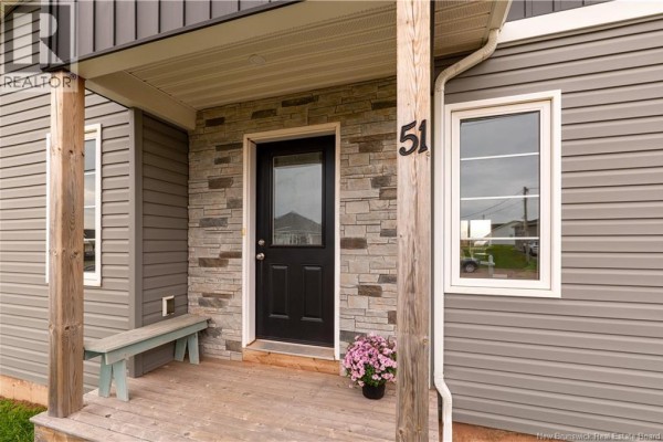 Close-up of the front entrance with a black door, stone veneer, wooden porch posts, and a light blue bench. - 51-53 Macintosh Boulevard, Moncton